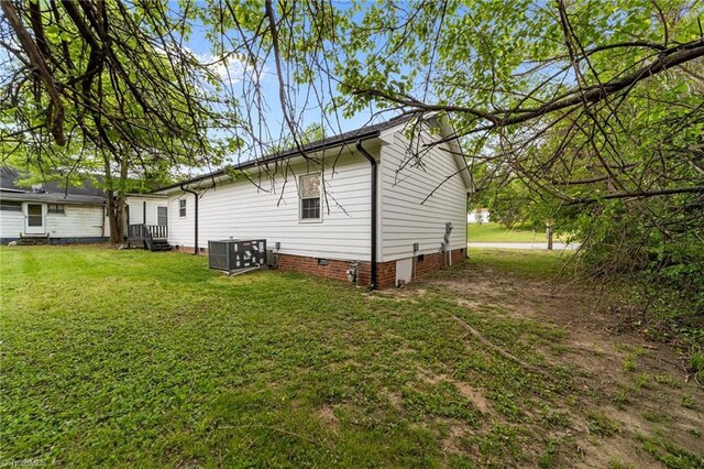 rear view of house with cooling unit, a lawn, and crawl space