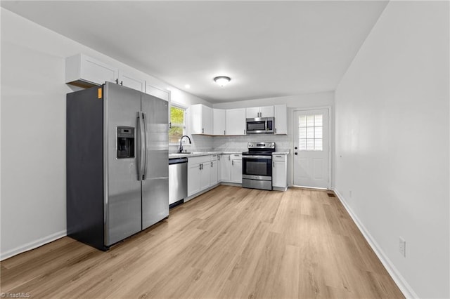 kitchen featuring stainless steel appliances, tasteful backsplash, light wood-style floors, white cabinetry, and light countertops