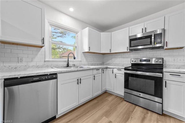 kitchen with white cabinetry, light wood finished floors, stainless steel appliances, and a sink