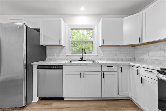 kitchen with stainless steel appliances, backsplash, a sink, light wood-style flooring, and white cabinetry