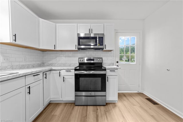 kitchen featuring white cabinets, light wood finished floors, stainless steel appliances, visible vents, and tasteful backsplash