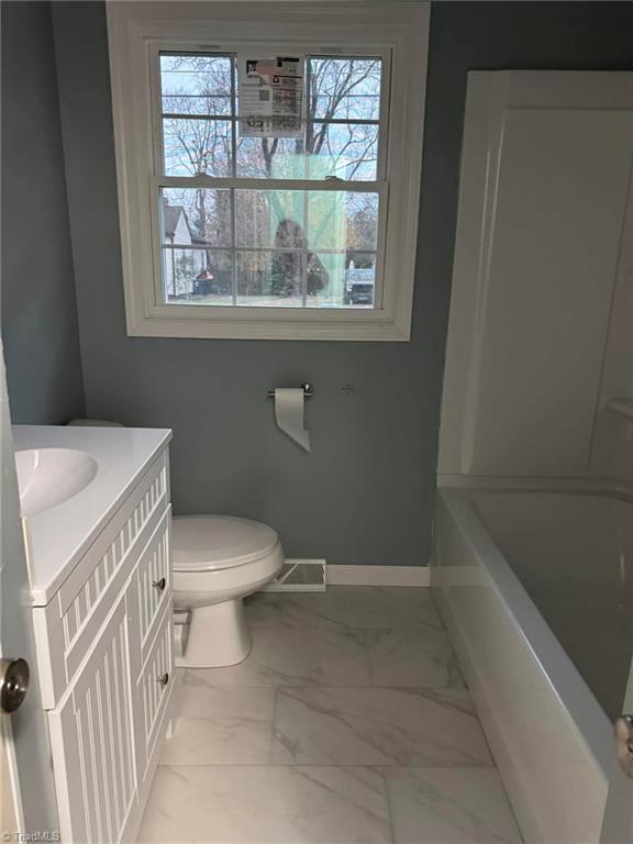 bathroom with vanity, a bathtub, toilet, and a wealth of natural light