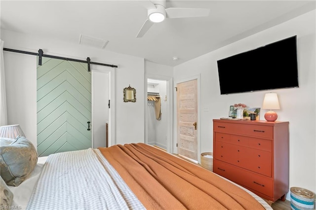 bedroom featuring a barn door, a ceiling fan, connected bathroom, a spacious closet, and a closet