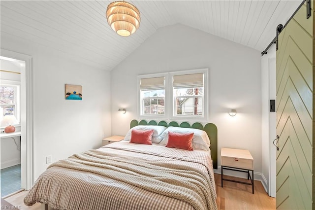 bedroom with light wood-style floors, vaulted ceiling, baseboards, and a barn door