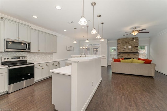 kitchen featuring crown molding, dark hardwood / wood-style floors, an island with sink, decorative light fixtures, and stainless steel appliances