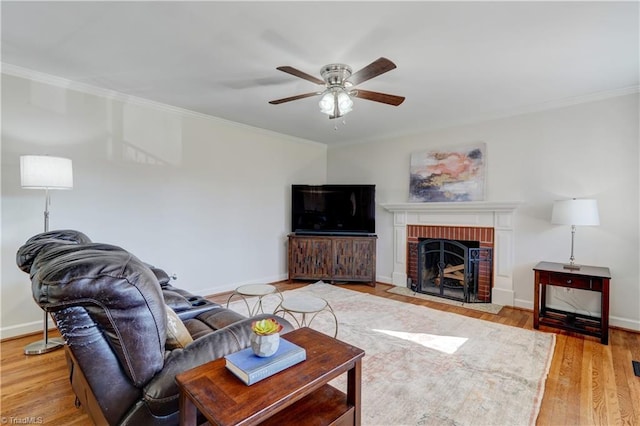 living room with crown molding, a fireplace, ceiling fan, and light wood-type flooring