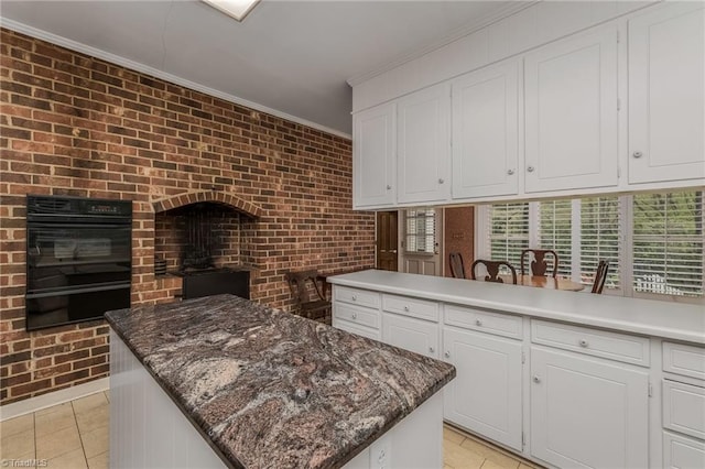 kitchen with light tile floors, white cabinets, ornamental molding, a kitchen island, and brick wall