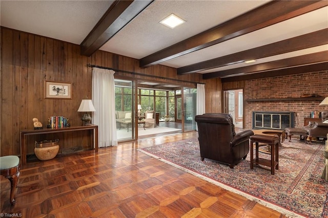 living room featuring dark parquet floors, wood walls, beamed ceiling, a fireplace, and a textured ceiling