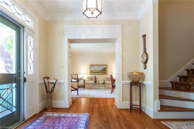 entryway with hardwood / wood-style floors, crown molding, and a notable chandelier