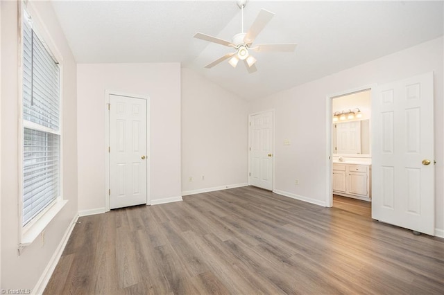 unfurnished bedroom featuring ensuite bath, a ceiling fan, baseboards, wood finished floors, and vaulted ceiling