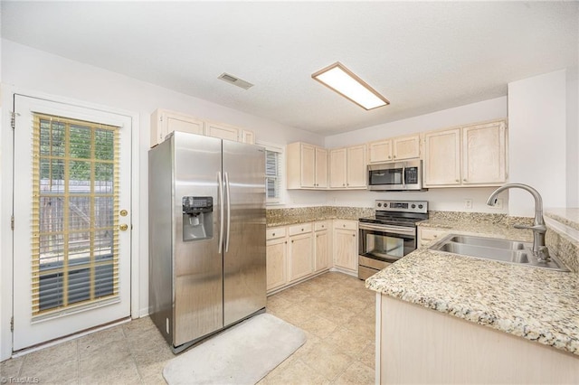 kitchen featuring visible vents, light brown cabinets, light stone counters, a sink, and stainless steel appliances
