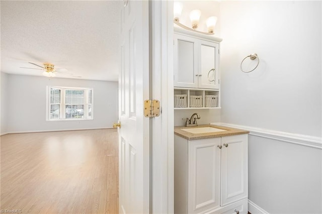 bathroom with a ceiling fan, a textured ceiling, wood finished floors, baseboards, and vanity