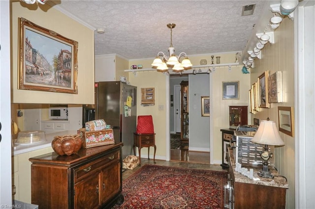 interior space featuring stainless steel refrigerator, hanging light fixtures, crown molding, a textured ceiling, and an inviting chandelier