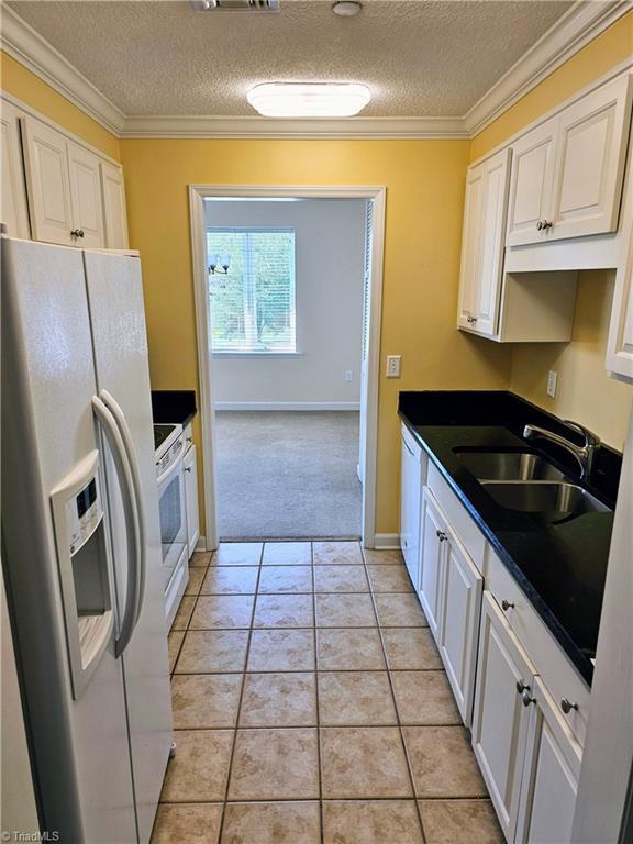 kitchen with light tile patterned floors, white appliances, a sink, dark countertops, and crown molding