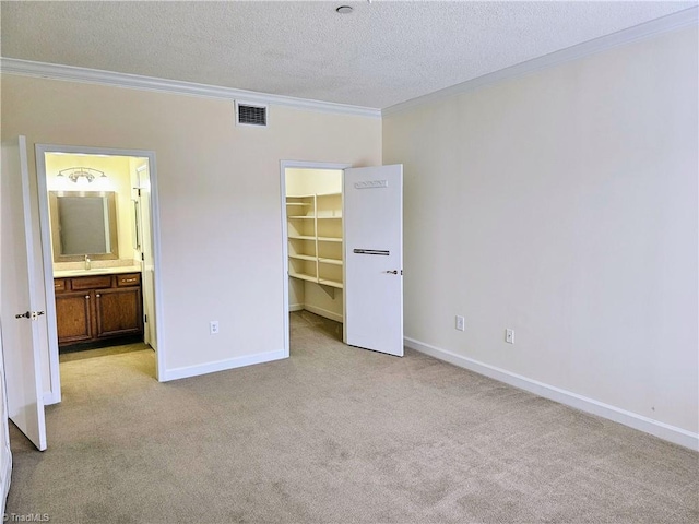 unfurnished bedroom with a textured ceiling, light carpet, crown molding, a walk in closet, and ensuite bath