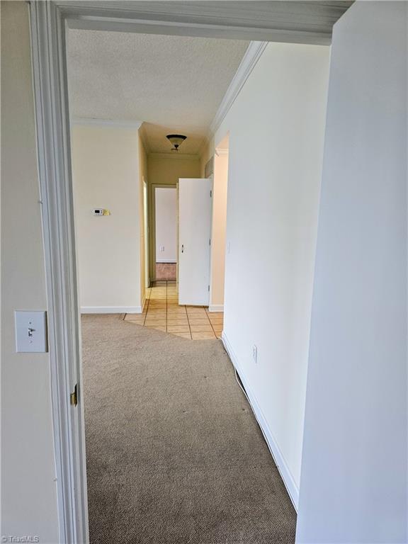 corridor with light carpet, a textured ceiling, and crown molding