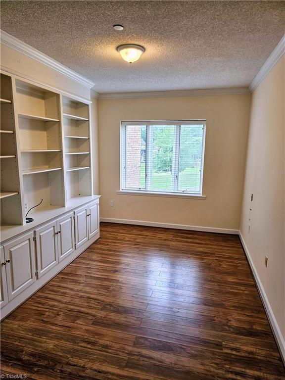 spare room featuring ornamental molding, dark wood-style flooring, a textured ceiling, and baseboards