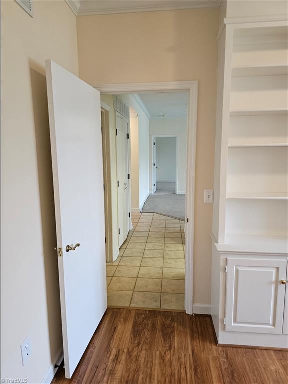 hallway featuring ornamental molding, built in shelves, baseboards, and wood finished floors