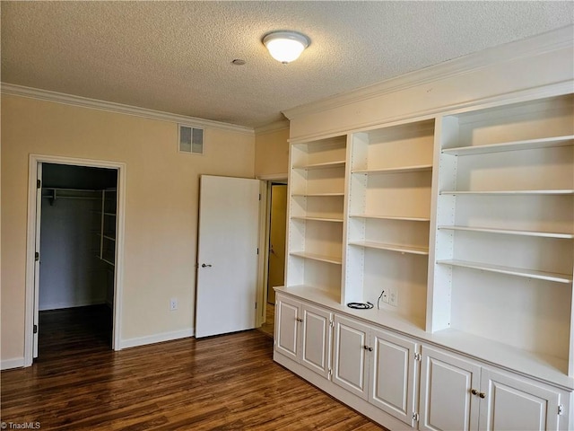 unfurnished bedroom featuring a walk in closet, a closet, visible vents, dark wood-type flooring, and ornamental molding