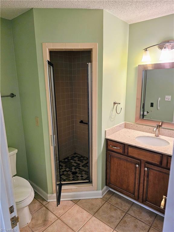 bathroom with toilet, a stall shower, a textured ceiling, vanity, and tile patterned floors