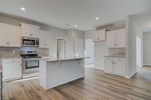 kitchen featuring light stone counters, a center island, backsplash, white cabinets, and appliances with stainless steel finishes