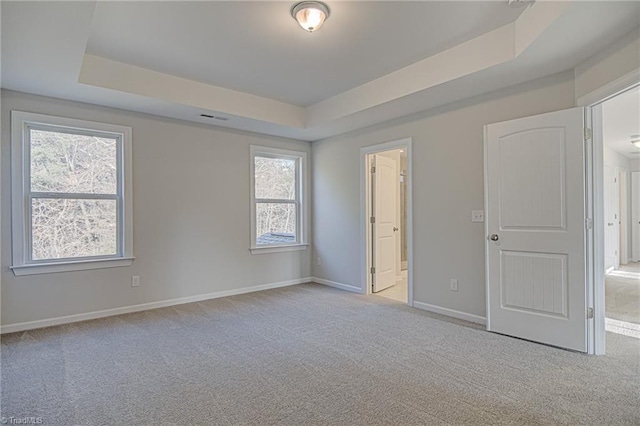 unfurnished bedroom featuring multiple windows, connected bathroom, a raised ceiling, and light colored carpet