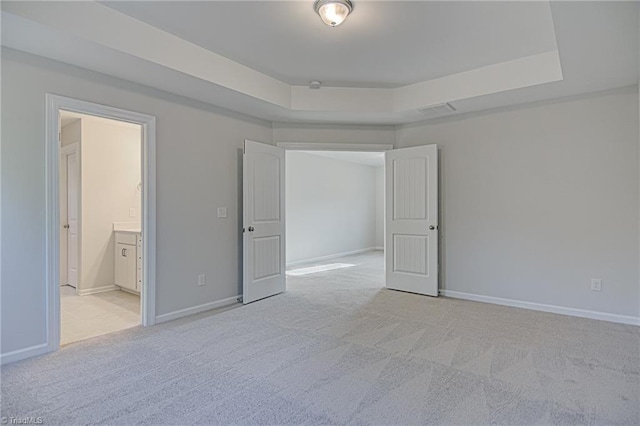 unfurnished bedroom with light colored carpet, a raised ceiling, and ensuite bath