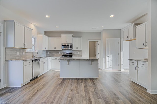 kitchen with light stone counters, stainless steel appliances, white cabinets, and a center island