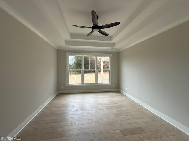 spare room featuring light hardwood / wood-style floors, ceiling fan, and a tray ceiling