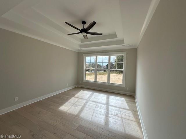 empty room with a raised ceiling, ceiling fan, and light hardwood / wood-style flooring