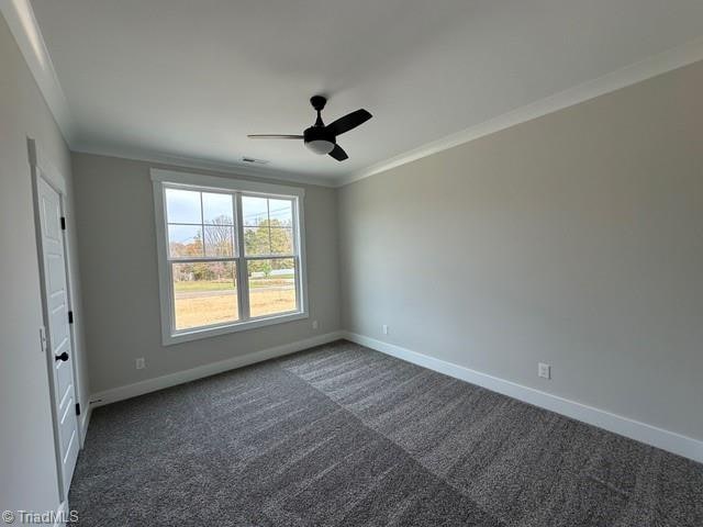 spare room featuring dark colored carpet, ceiling fan, and ornamental molding