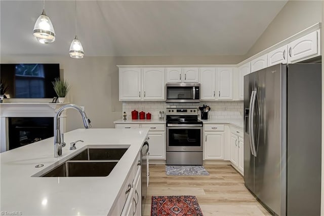 kitchen featuring white cabinets, stainless steel appliances, decorative backsplash, sink, and hanging light fixtures