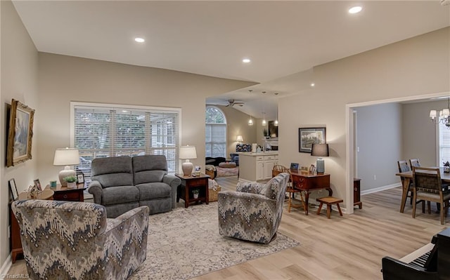 living room with ceiling fan with notable chandelier and light hardwood / wood-style flooring