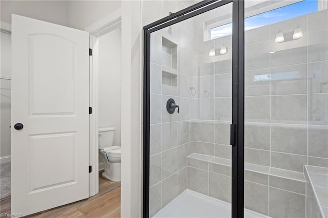 bathroom with hardwood / wood-style floors, a shower with shower door, and toilet