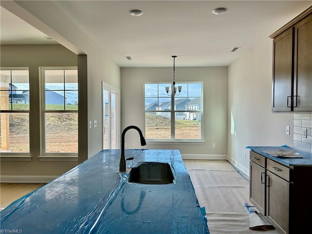 kitchen with pendant lighting, sink, dark stone countertops, an inviting chandelier, and dark brown cabinets