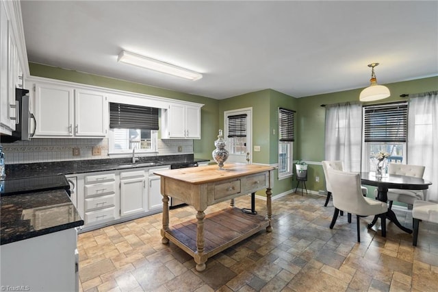 kitchen with stone tile floors, white cabinets, backsplash, and a sink