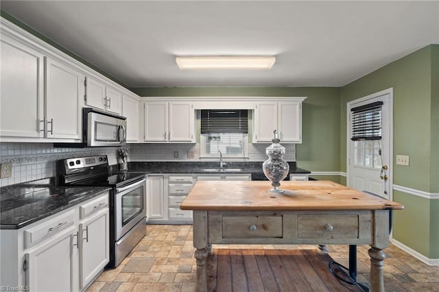 kitchen with stone finish flooring, decorative backsplash, appliances with stainless steel finishes, white cabinetry, and a sink