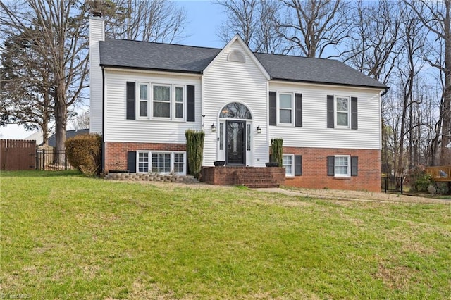 bi-level home featuring brick siding, a chimney, a front lawn, and fence