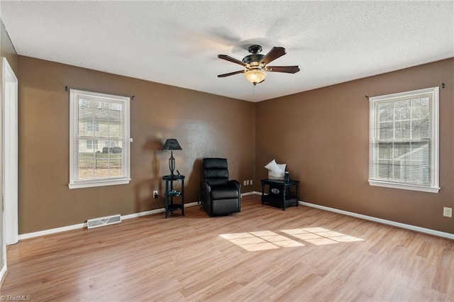 living area with visible vents, a textured ceiling, a ceiling fan, and light wood finished floors