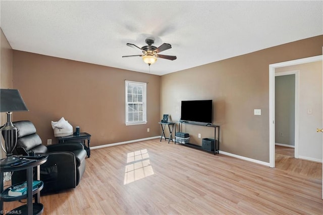 living area with a textured ceiling, light wood-style floors, baseboards, and ceiling fan