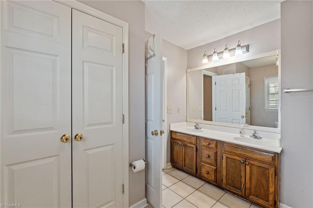 full bathroom with double vanity, tile patterned flooring, a textured ceiling, and a sink