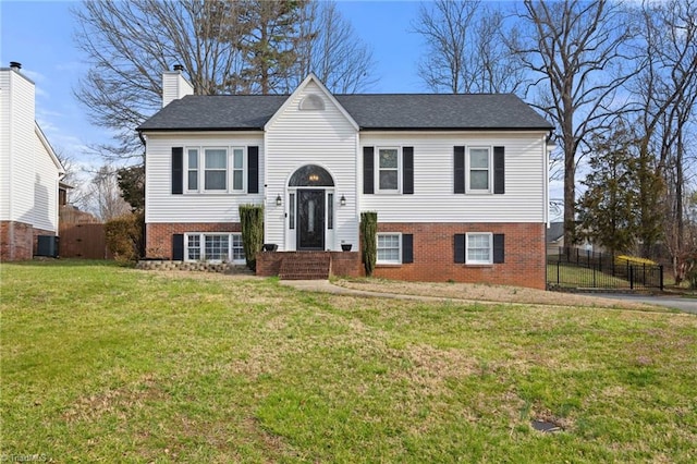 bi-level home with brick siding, a shingled roof, fence, a front yard, and a chimney