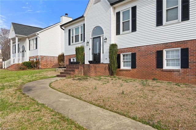 bi-level home featuring brick siding, a front lawn, and a chimney