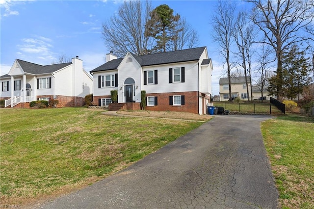 bi-level home featuring brick siding, a front yard, driveway, and fence