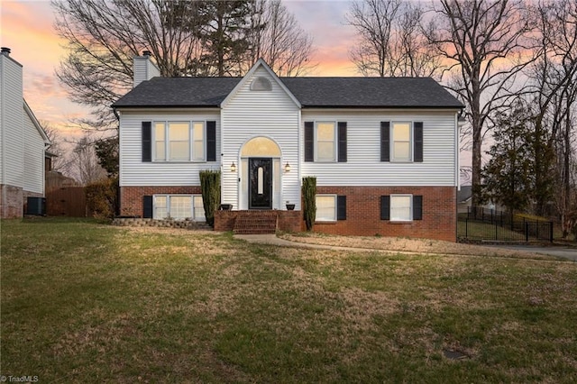 raised ranch with a yard, fence, brick siding, and a chimney