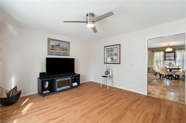 living room with light wood finished floors, baseboards, and a ceiling fan