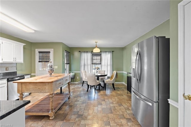 kitchen featuring baseboards, decorative backsplash, white cabinets, appliances with stainless steel finishes, and stone finish flooring