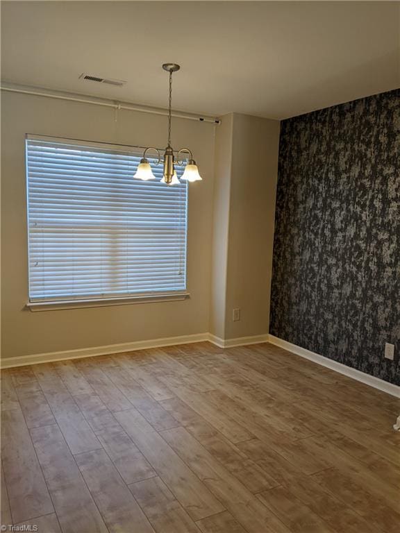 unfurnished dining area with a notable chandelier, visible vents, an accent wall, wood finished floors, and baseboards