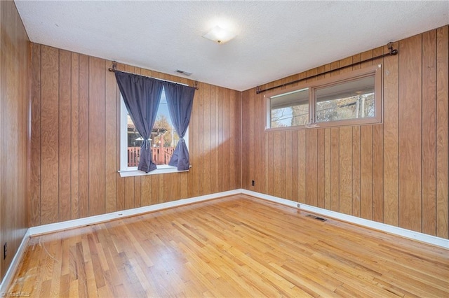 empty room with hardwood / wood-style flooring, wood walls, and a textured ceiling