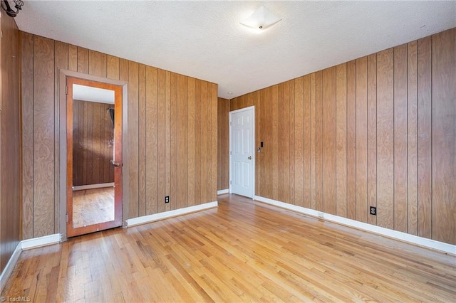 spare room with a textured ceiling, light hardwood / wood-style flooring, and wood walls